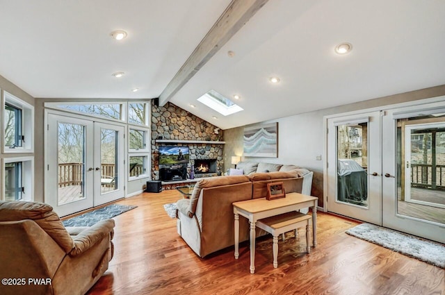 living room with french doors, light wood-type flooring, lofted ceiling with skylight, a fireplace, and plenty of natural light