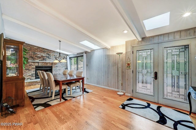 interior space with light hardwood / wood-style flooring, a brick fireplace, wooden walls, and vaulted ceiling with skylight