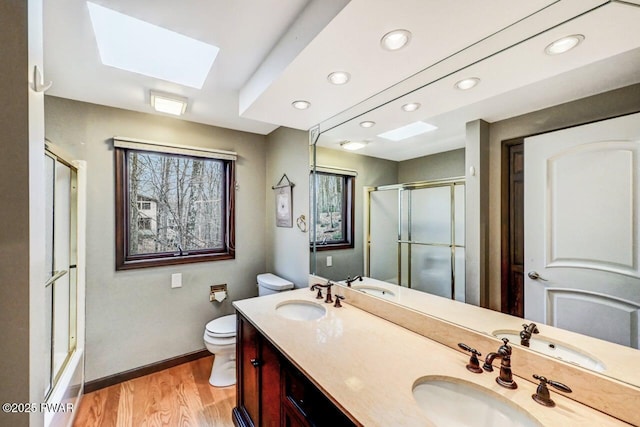 full bathroom featuring vanity, a skylight, toilet, enclosed tub / shower combo, and wood-type flooring