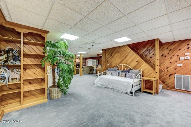 unfurnished bedroom with a paneled ceiling, wood walls, and carpet floors