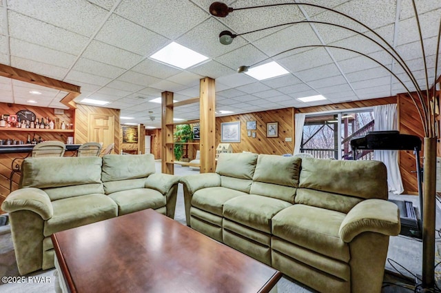 living room featuring a paneled ceiling and wood walls