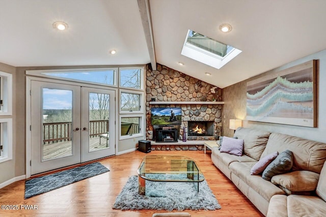 living room with a fireplace, lofted ceiling with skylight, light hardwood / wood-style flooring, and french doors