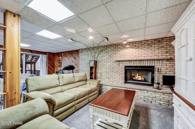 living room with a paneled ceiling, wooden walls, a fireplace, and concrete floors