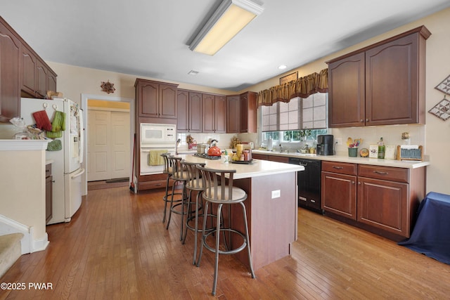 kitchen with a breakfast bar, white appliances, wood-type flooring, light countertops, and a center island