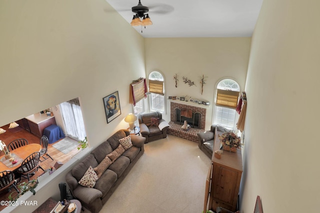 living room featuring high vaulted ceiling, ceiling fan, a brick fireplace, and carpet flooring
