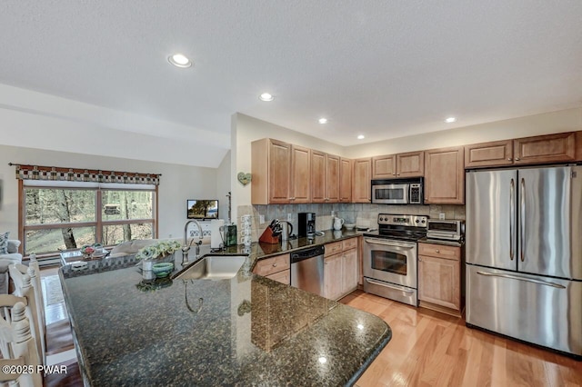 kitchen with a sink, backsplash, light wood-style floors, appliances with stainless steel finishes, and a peninsula