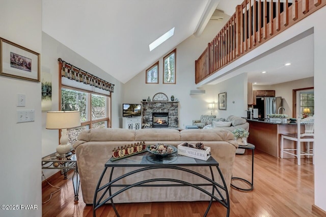 living room with high vaulted ceiling, light wood-style flooring, a wall unit AC, a stone fireplace, and a skylight