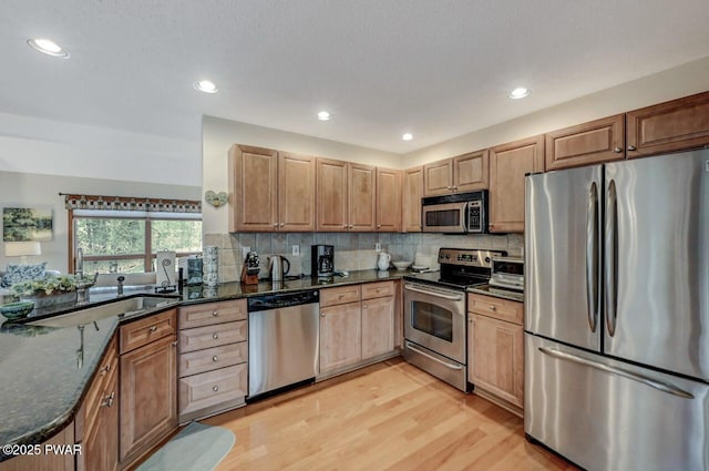 kitchen with decorative backsplash, light wood-style flooring, stainless steel appliances, and dark stone counters