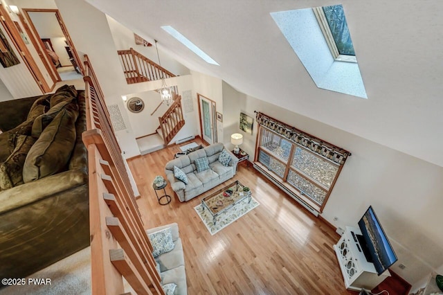 living room featuring high vaulted ceiling, stairway, a skylight, and wood finished floors