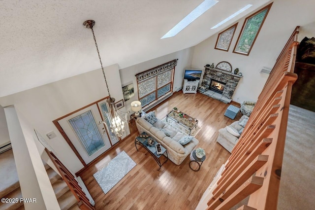 living area featuring wood finished floors, vaulted ceiling with skylight, a fireplace, a textured ceiling, and a notable chandelier