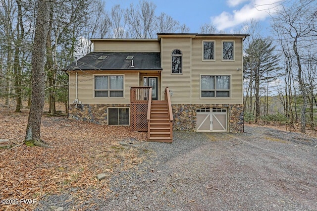 view of front of home featuring stairs, stone siding, gravel driveway, and an attached garage