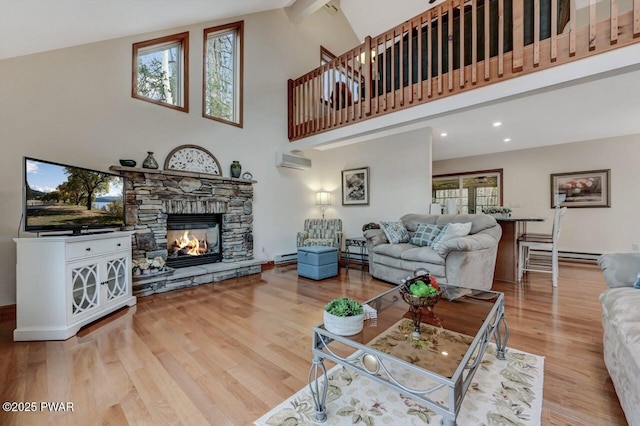 living area featuring wood finished floors, a wall unit AC, a high ceiling, a stone fireplace, and a baseboard radiator