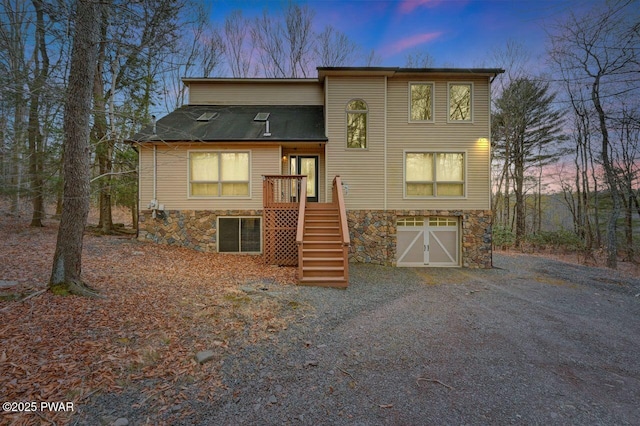 view of front of property featuring a garage, stone siding, gravel driveway, and stairway