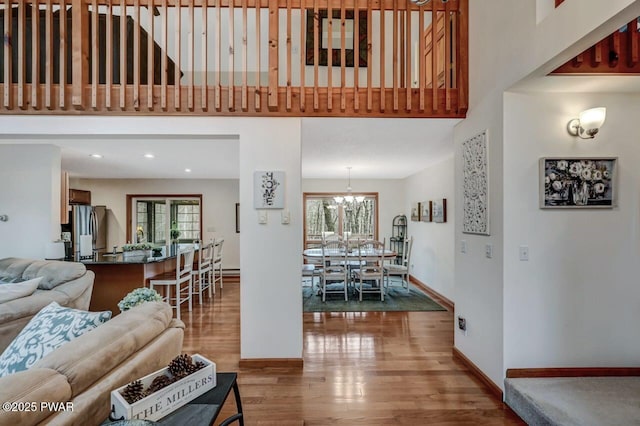 living room featuring baseboards, recessed lighting, a high ceiling, wood finished floors, and a notable chandelier