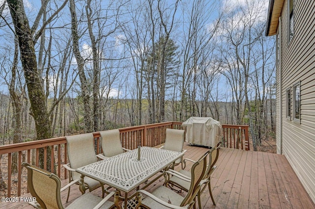 deck featuring outdoor dining area, a view of trees, and a grill