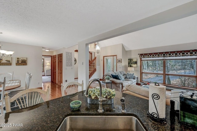 kitchen featuring a sink, a textured ceiling, dark stone countertops, and a chandelier