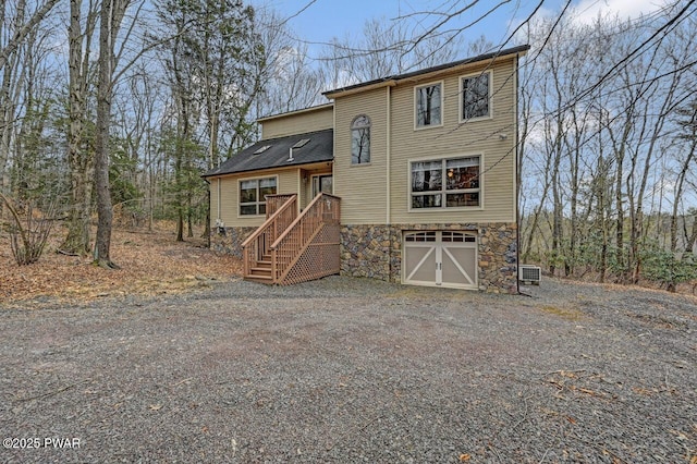 chalet / cabin featuring stone siding, an attached garage, and gravel driveway