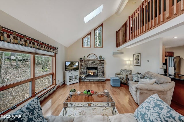 living area featuring high vaulted ceiling, a skylight, a stone fireplace, and wood finished floors