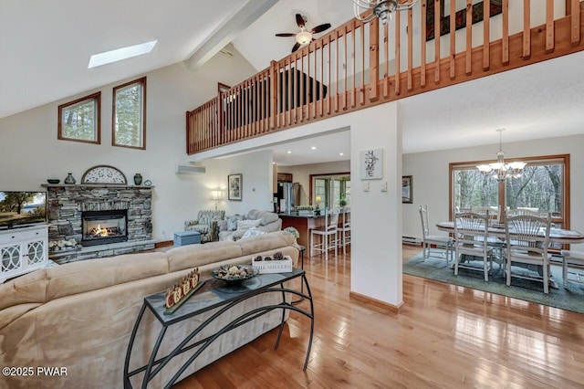 living room with light wood finished floors, beam ceiling, a fireplace, a wall mounted air conditioner, and ceiling fan with notable chandelier