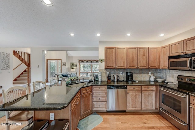 kitchen with dark stone counters, a sink, appliances with stainless steel finishes, a kitchen bar, and tasteful backsplash