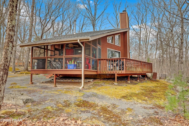 rear view of property featuring a chimney, a shingled roof, a deck, and a sunroom