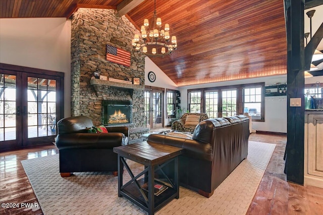 living room with high vaulted ceiling, french doors, a stone fireplace, a notable chandelier, and light hardwood / wood-style floors