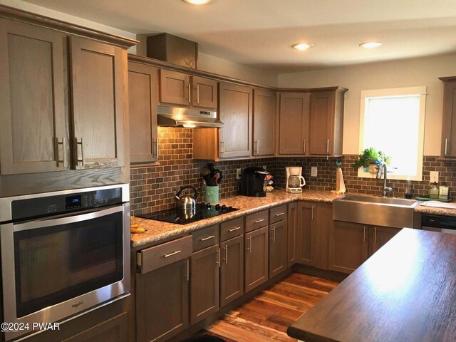 kitchen with a sink, black electric stovetop, under cabinet range hood, stainless steel oven, and backsplash