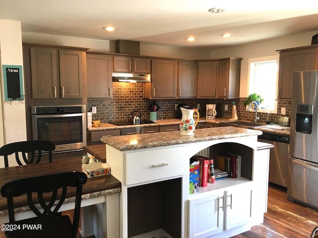 kitchen featuring a center island, stainless steel appliances, tasteful backsplash, a sink, and under cabinet range hood