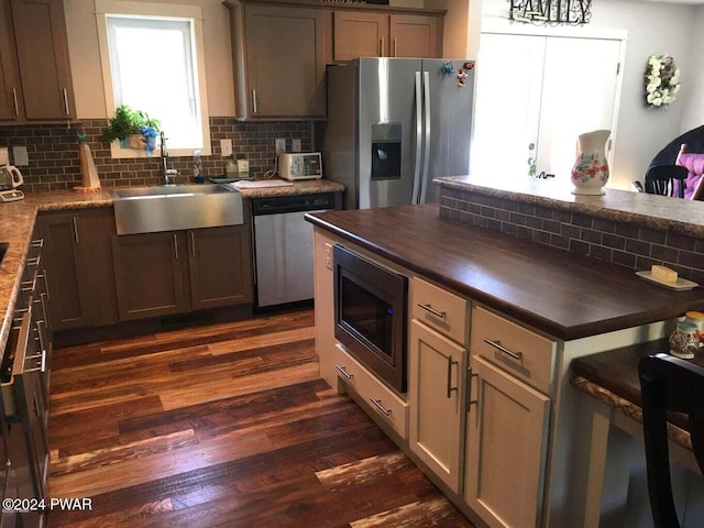 kitchen featuring dark wood finished floors, decorative backsplash, butcher block countertops, stainless steel appliances, and a sink