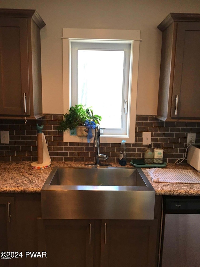 kitchen with dark brown cabinets, stainless steel dishwasher, a sink, and decorative backsplash