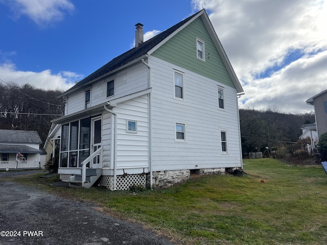 view of property exterior featuring a yard, a chimney, and a sunroom