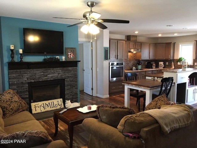 living room featuring baseboards, a ceiling fan, dark wood-type flooring, a stone fireplace, and recessed lighting