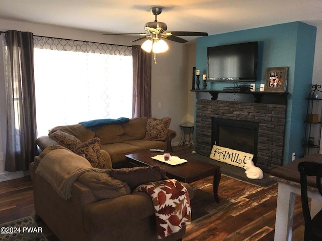 living area featuring ceiling fan, dark wood-type flooring, and a stone fireplace