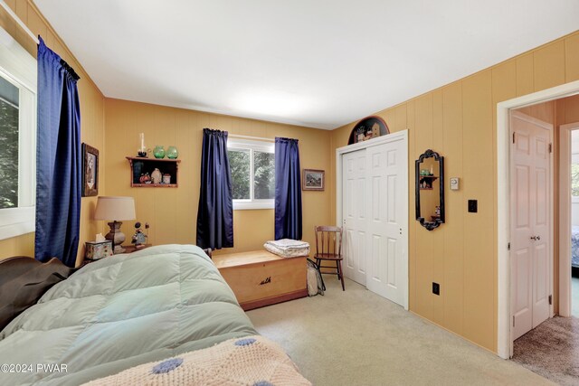 bedroom featuring light carpet, wooden walls, and a closet