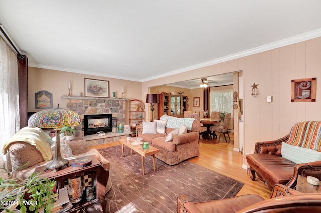 living room featuring a stone fireplace, crown molding, ceiling fan, and wood-type flooring