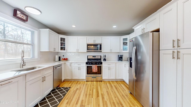 kitchen featuring decorative backsplash, stainless steel appliances, sink, light hardwood / wood-style floors, and white cabinetry