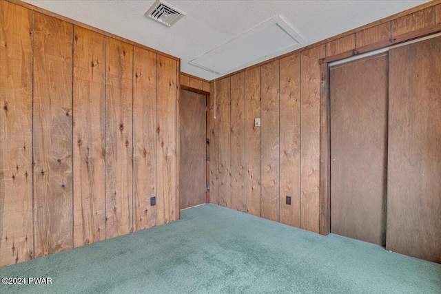 carpeted spare room with wood walls and a textured ceiling