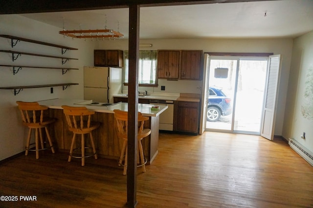 kitchen with light countertops, brown cabinetry, freestanding refrigerator, dishwasher, and a peninsula