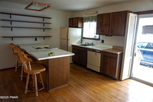 kitchen with a breakfast bar area, white appliances, a sink, light countertops, and open shelves