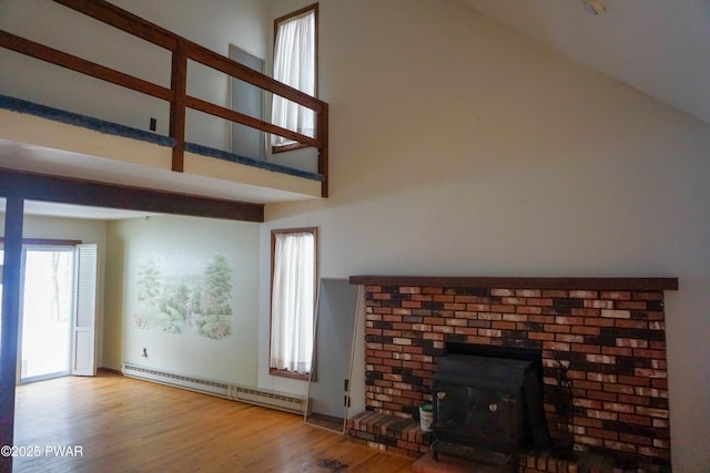 unfurnished living room featuring a baseboard heating unit, a wood stove, a towering ceiling, and wood finished floors