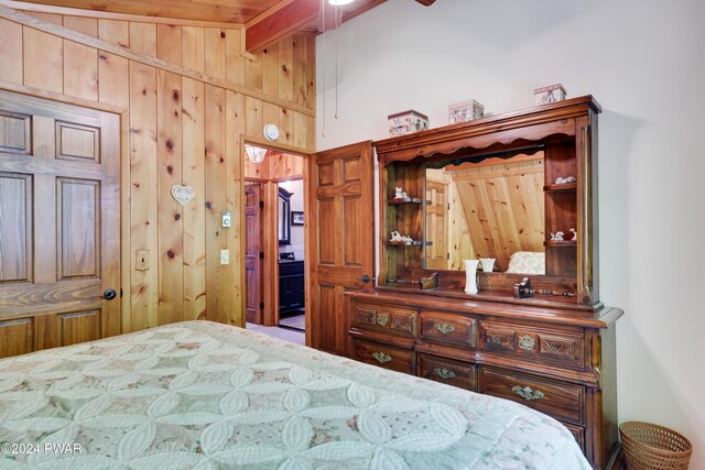 bedroom with ensuite bathroom, wood walls, and beam ceiling