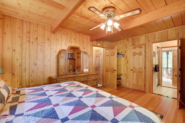 unfurnished bedroom with wood walls, light hardwood / wood-style flooring, ceiling fan, and beamed ceiling