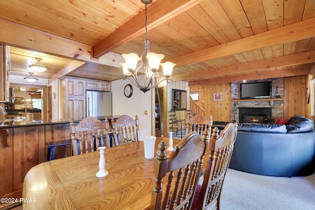 dining room featuring wood walls, wooden ceiling, a brick fireplace, beam ceiling, and a chandelier