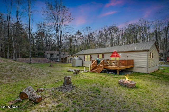78 Orion Way, Lake Ariel, PA 18436 - back of house at dusk with an outdoor fire pit, a deck, a lawn, a storage unit, and view of wooded area