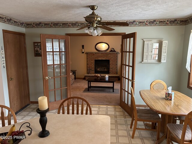 dining area featuring ceiling fan, french doors, a textured ceiling, and a brick fireplace