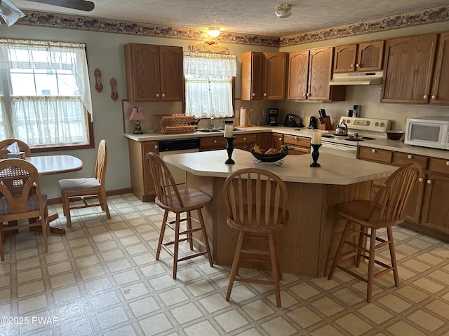 kitchen with a breakfast bar, a kitchen island, white appliances, and sink