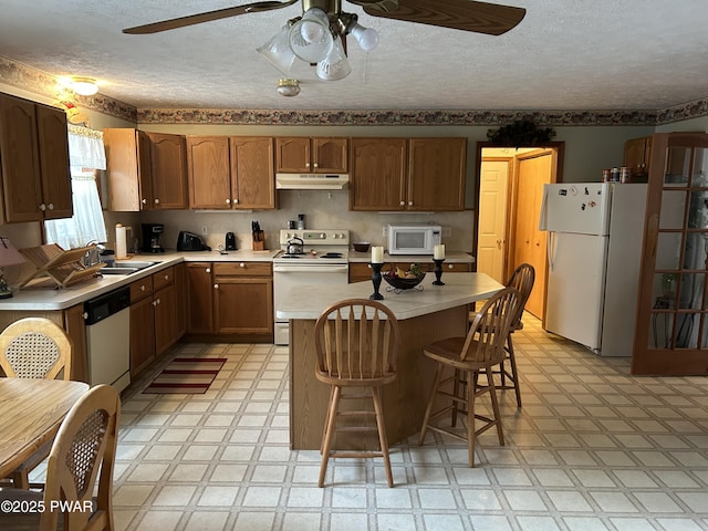 kitchen featuring a breakfast bar, a textured ceiling, white appliances, sink, and a center island