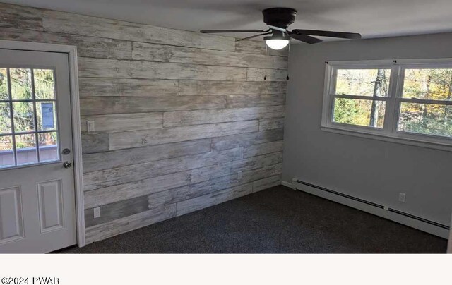 spare room with a healthy amount of sunlight, ceiling fan, a baseboard radiator, and wood walls