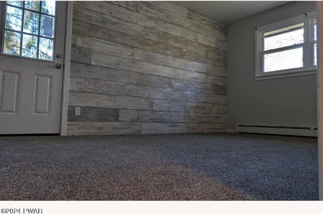 unfurnished room featuring wooden walls, a wealth of natural light, and a baseboard heating unit