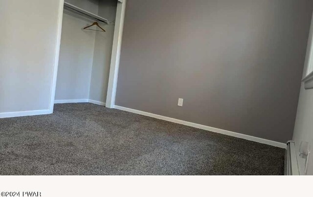 unfurnished bedroom featuring dark carpet, a closet, and a baseboard heating unit